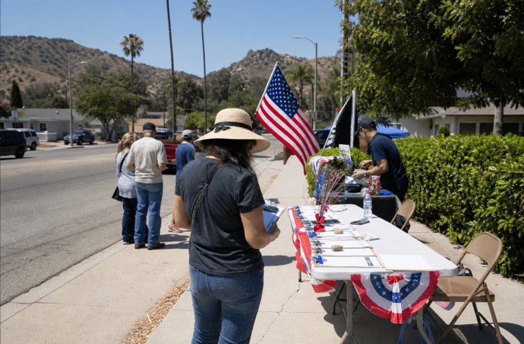 Volunteers at an outdoor table with American flags and clipboards